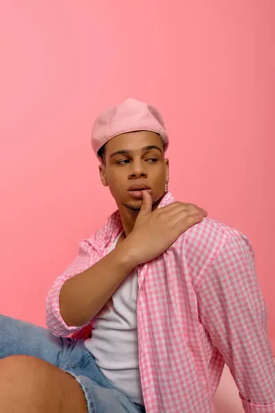 Un joven negro exhibe su elegante camisa a cuadros sobre un fondo rosa. - foto de stock