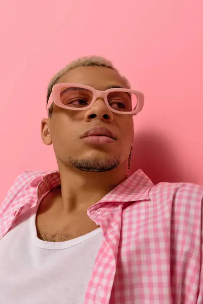 A young Black man with dyed hair poses confidently in a checkered shirt against a pink backdrop. — Stock Photo
