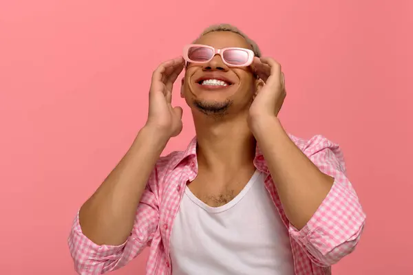 Un giovane afroamericano posa fiducioso, sorridendo con gli occhiali da sole e una camicia a scacchi. — Foto stock