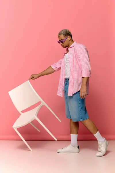 Un giovane afroamericano posa fiducioso con una sedia, mostrando il suo stile alla moda. — Foto stock