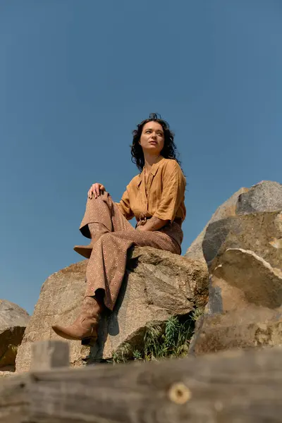 Curly-haired woman poses confidently on rocks outdoors, embracing summer vibes in her outfit. — Stock Photo