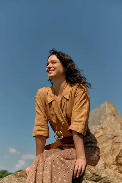A cheerful woman with curly hair poses on a rock, enjoying summer warmth in style. — стоковое фото