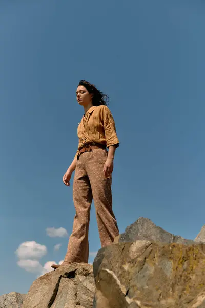 A young woman with curly hair confidently poses on a rocky outcrop under a clear blue sky. — стоковое фото