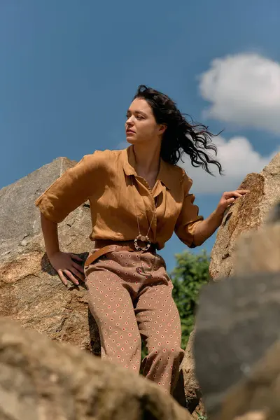 Curly-haired woman poses confidently among rocks under a clear blue sky. — стоковое фото
