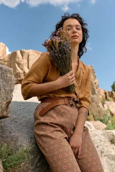 A young woman with curly hair poses outdoors holding flowers, showcasing her summer style. — стоковое фото