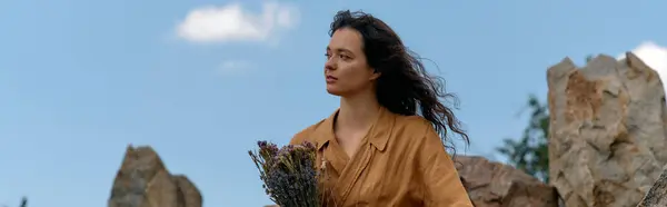 Wearing a trendy summer outfit, a young woman stands outdoors, holding flowers with confidence, banner — стоковое фото
