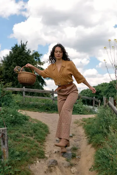 Curly-haired woman strolls along a scenic path while carrying a basket on a sunny summer day. — Stock Photo