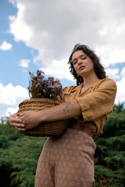 A confident young woman with curly hair enjoys summer outdoors, posing with flowers. — стоковое фото