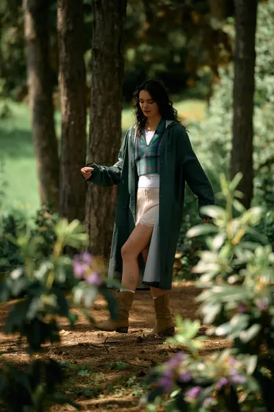 A young woman with curly hair explores the vibrant summer forest in stylish attire. — стоковое фото