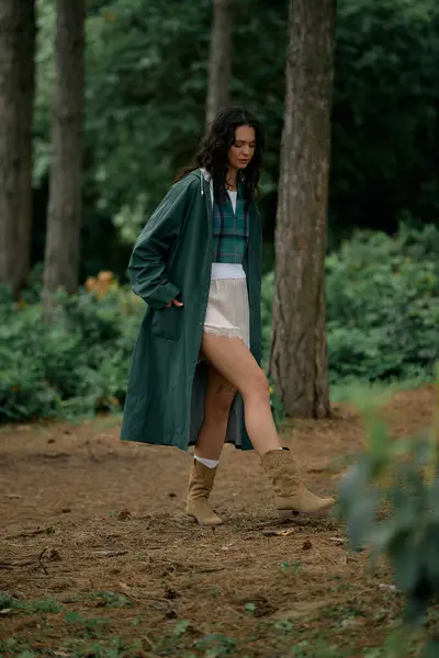 A young woman in a chic raincoat strolls gracefully through a vibrant green forest. — Stock Photo
