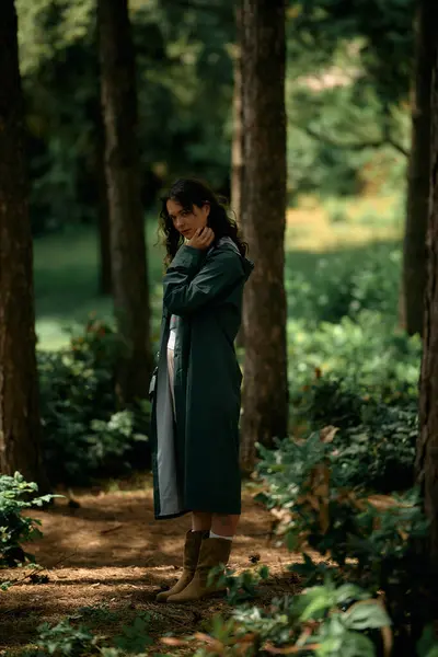 Curly-haired woman enjoys the serenity of a lush forest while wearing a fashionable raincoat. — стоковое фото