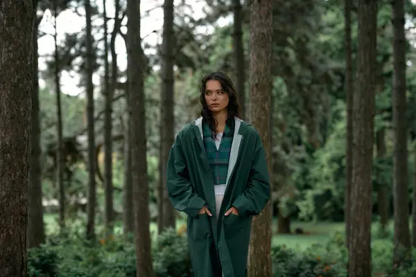 A young woman with curly hair wears a trendy raincoat while exploring lush greenery in summer. — стоковое фото