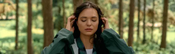 Mujer de pelo rizado abraza la naturaleza en un bosque vibrante mientras usa un impermeable llamativo, pancarta - foto de stock