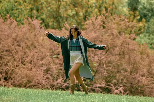 Curly-haired woman enjoys a carefree moment outdoors in a fashionable raincoat during summer. — Stock Photo