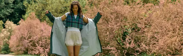 Curly-haired woman showcases a trendy raincoat while enjoying the outdoors in summer, banner — Stock Photo