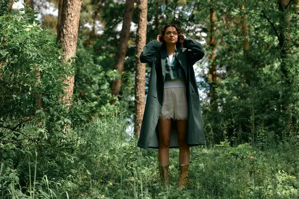 Curly-haired woman showcases her fashion sense in a stylish raincoat while outdoors in the woods. — стоковое фото