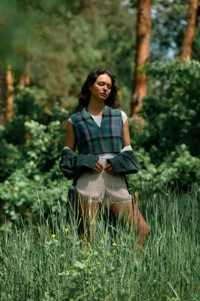 A young woman poses gracefully in a trendy raincoat amidst lush greenery on a warm summer day. — стоковое фото