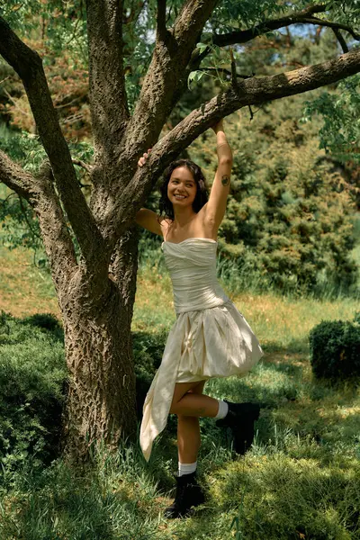 A young woman with curly hair poses joyfully by a tree in a beautiful summer setting. — Stock Photo