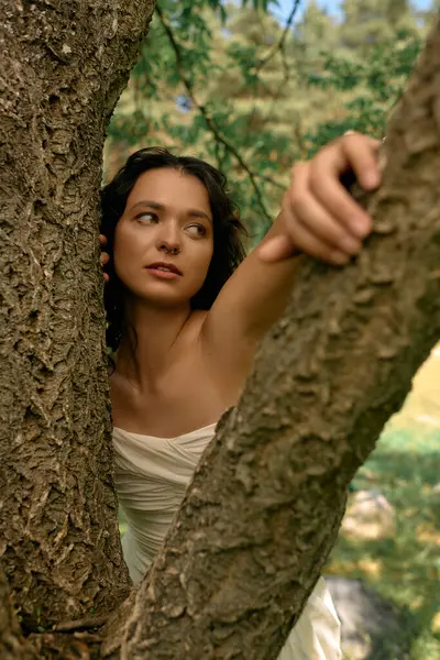 Mujer joven con el pelo rizado posa con gracia en un vestido blanco entre los árboles en un día soleado de verano. - foto de stock