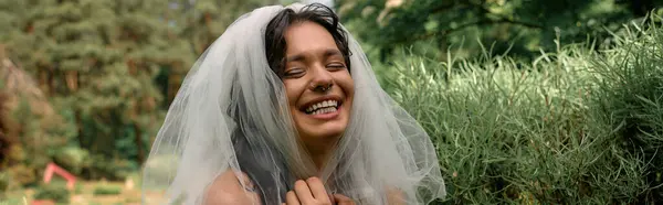 A young bride in a flowing white veil smiles outdoors on a sunny day, banner — стоковое фото
