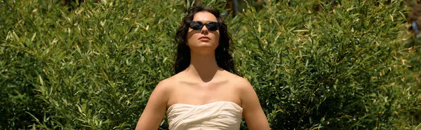 A young woman in a white dress poses confidently outdoors under the summer sun, banner — стоковое фото