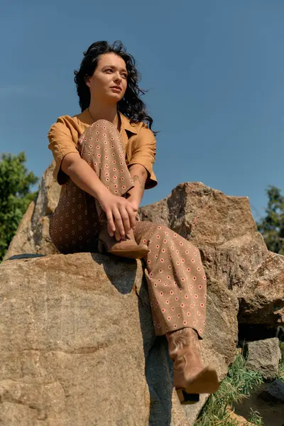 Curly-haired woman poses on a rock, confident and radiant under the blue sky in summer style. — Fotografia de Stock