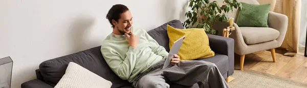 Impegnato nel tempo libero, un giovane bell'uomo si rilassa su un accogliente divano mentre utilizza un tablet nella sua casa. — Foto stock