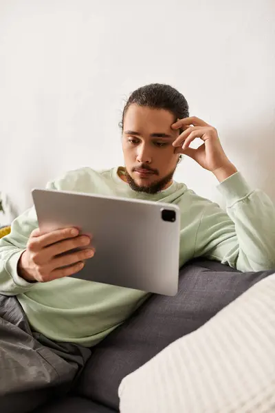 Young handsome man sits comfortably at home, focused on a tablet screen while relaxing. — Stock Photo