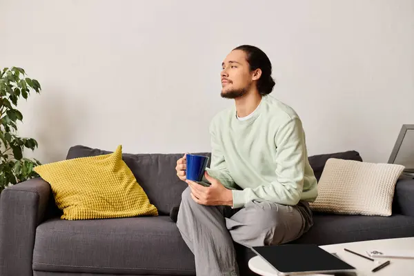 Un giovane rilassato siede su un accogliente divano, assaporando il suo drink mentre contemplava la vita. — Foto stock