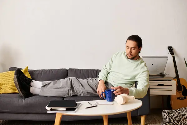 Un giovane uomo si rilassa su un divano, assaporando il suo drink nel comfort di casa. — Foto stock