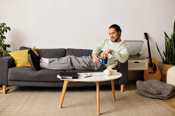 A young handsome man lounges comfortably on a couch, sipping from a can while relaxing. — Stock Photo