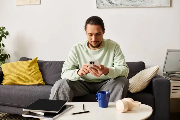 A young man relaxes in a cozy living room, sipping coffee and using his smartphone. — Stock Photo