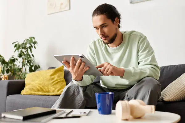 A young handsome man is sitting at home focused on his tablet, surrounded by cozy decor. — Stock Photo