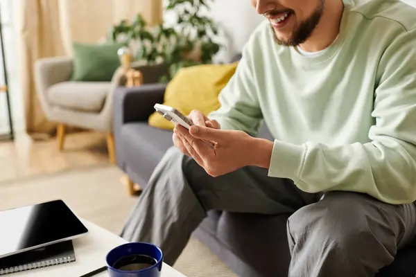 Man relaxes at home, smiling as he interacts with his smartphone, creating a warm ambiance. — Stock Photo
