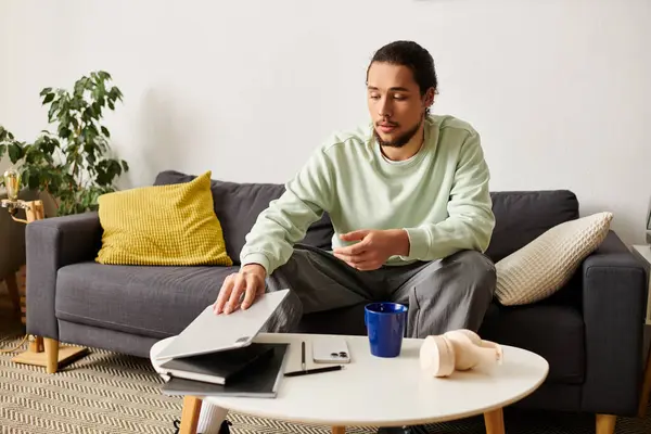 A young man sits comfortably on his couch, focused on his laptop and sipping from a blue cup. — Stock Photo