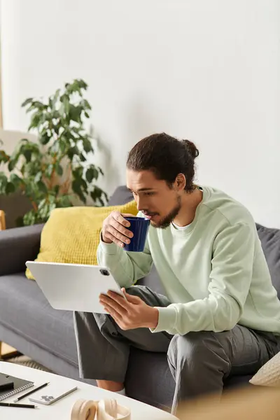Young man enjoys a cozy afternoon at home while sipping a warm drink and browsing online. — Stock Photo