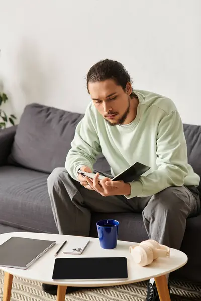Young man sits comfortably at home, engaged with his smartphone while surrounded by casual decor. — Stock Photo