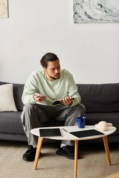 A young handsome man engages with gadgets while relaxing on a comfortable sofa in his living room. — Stock Photo