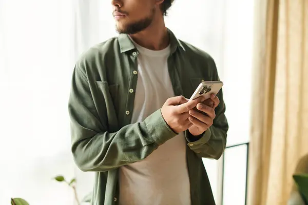 A young man at home holds a smartphone, basking in soft morning light. — Stock Photo