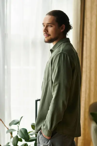 Bright natural light fills a cozy room as a young man stands thoughtfully by the window. — Stock Photo