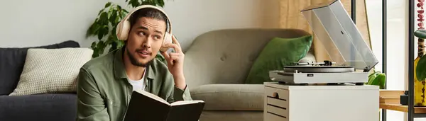 A young man relaxes at home, reading a book and enjoying music. — Stock Photo