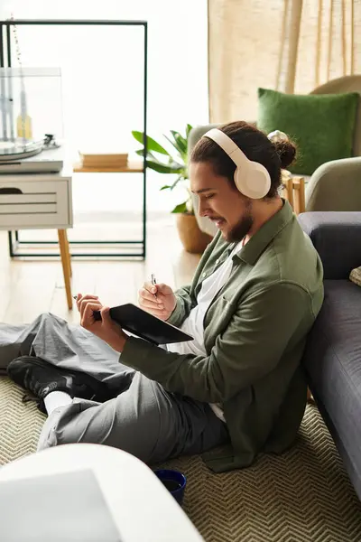 Relaxing at home, young man enjoys creative moments while sketching with headphones on. — Stock Photo