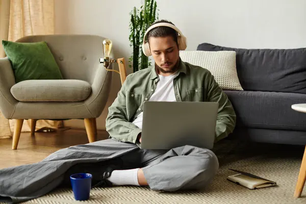 Young man sits comfortably on the floor, focused on his laptop with a drink nearby. — Stock Photo