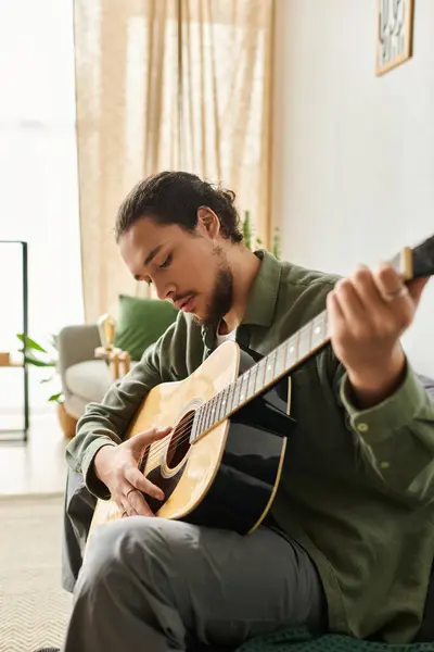 In a relaxed atmosphere, a young man strums his acoustic guitar, lost in the music at home. — Stock Photo