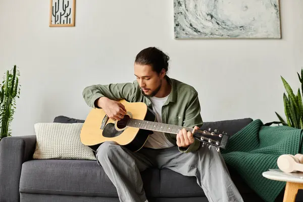 A young man strums his guitar in a comfortable living space, surrounded by greenery and art. — Stock Photo