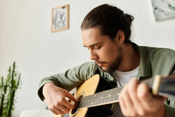 A young man plays guitar in his cozy home, lost in the notes and expression of music. — Stock Photo