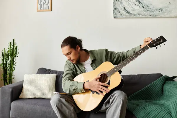 Handsome young man at home sits on a couch, strumming a guitar and savoring a quiet moment. — Stock Photo
