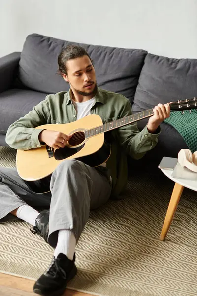 Schöner junger Mann sitzt gemütlich auf Teppich, spielt Gitarre und genießt ruhigen Nachmittag zu Hause. — Stockfoto