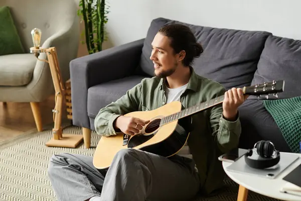 Schöner junger Mann entspannt zu Hause, spielt eine Gitarre und schafft eine beruhigende Atmosphäre. — Stockfoto