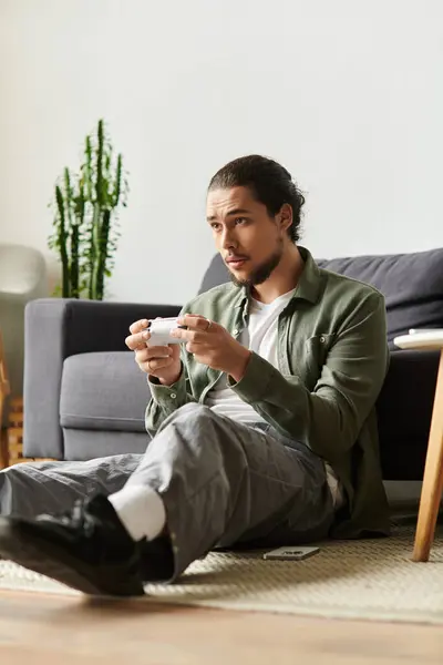 Un giovane si siede comodamente sul pavimento, assaporando il suo drink mentre è immerso nel pensiero. — Foto stock